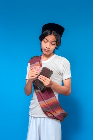 A traditional Indonesian man in a sarong and peci looks uncertain while putting rupiah banknotes...