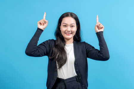 Smiling woman raising both index fingers upward against blue background, presenting or highlighting copy space. Ideal for business, advertising, and promotional content.の写真素材