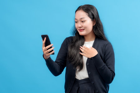 Happy young woman using smartphone, smiling with joy, symbolizing connectivity, modern communication, and technology, against a vibrant blue backgroundの写真素材