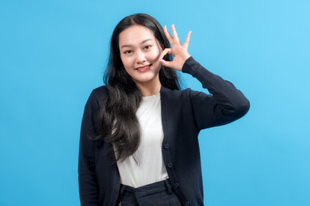 Confident young woman expressing positivity with a hand gesture, posing against a vivid background. Ideal for concepts like optimism, communication, and stylistic portrait photography.の写真素材