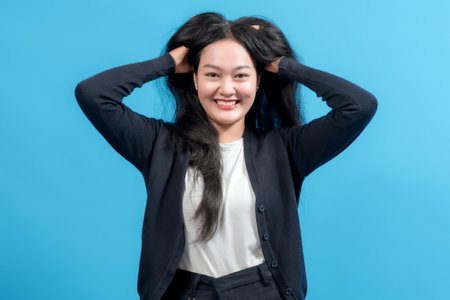 Woman in casual clothing pulling hair with stressed expression, standing against blue background.の写真素材