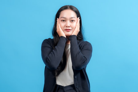Portrait of a woman with a thoughtful expression, standing against a vibrant blue background and resting her hands on her face, evoking calmness and contemplation.の写真素材