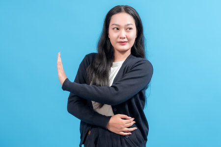 A young woman with long black hair is holding her hand up in a stop gesture against a bright blue background, conveying a message of pause or caution.の写真素材