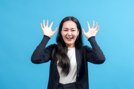 Frustrated woman with hands raised against blue background, showing stress, confusion, and strong emotions. Perfect for concepts of anxiety, pressure, or emotional struggle.の写真素材