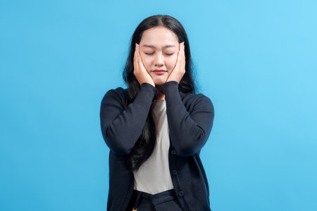 Portrait of a woman with a thoughtful expression, standing against a vibrant blue background and resting her hands on her face, evoking calmness and contemplation.の写真素材