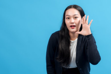 Happy woman making hand gesture near mouth, speaking or shouting, against blue background. Ideal for communication, announcements, and advertising concepts.の写真素材