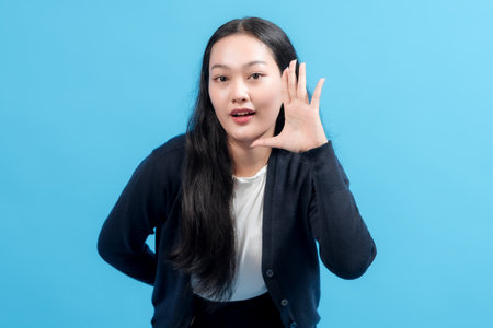 Happy woman making hand gesture near mouth, speaking or shouting, against blue background. Ideal for communication, announcements, and advertising concepts.の写真素材