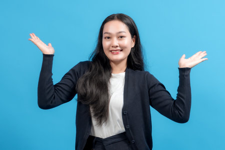 Smiling woman in casual outfit with open hand gesture, against a blue background, expressing positivity, welcoming, and friendly attitude. Perfect for business, communication, and support themes.の写真素材