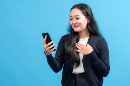 Happy young woman using smartphone, smiling with joy, symbolizing connectivity, modern communication, and technology, against a vibrant blue backgroundの写真素材