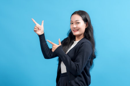 Smiling woman pointing with both hands against blue background. Positive gesture showing direction or presenting an idea. Perfect for business, marketing, and promotional themes.の写真素材