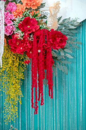 Vibrant floral decoration featuring red, pink, orange, white, and yellow blossoms with cascading textures on a turquoise striped backdrop, creating a festive and elegant celebration design.の写真素材