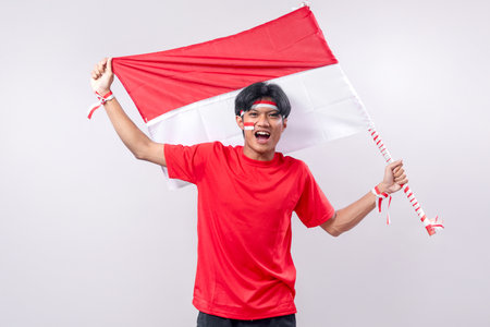 A joyful young Indonesian man waves the Indonesian flag with excitement, celebrating Independence...
