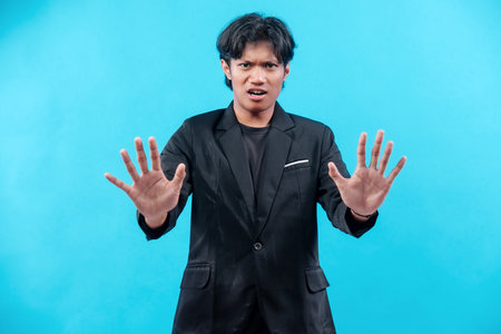A young man in a black suit raises both hands forward with a serious expression, showing a stop gesture that conveys warning, authority, and professional communication.の写真素材