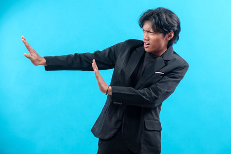 A young man in a black suit stretches his arms sideways with a serious face, showing a defensive...