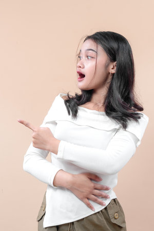 A surprised young Asian woman pointing sideways with expressive face, showing excitement and curiosity, perfect for concepts of discovery and attention.の写真素材