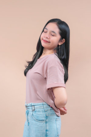 Asian woman with long black hair wearing a pastel casual t-shirt and light denim jeans, smiling with...