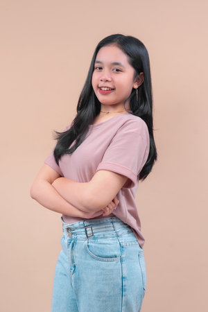 Asian woman with long black hair wearing a pastel t-shirt and denim jeans, standing confidently with...