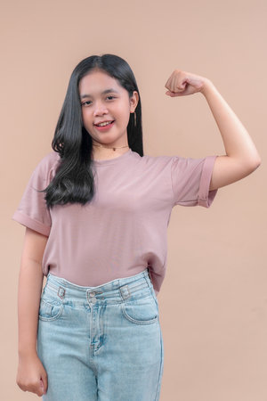 Asian woman in casual modern outfit confidently flexes her arm, wearing a pastel t-shirt and denim...