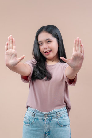 Asian woman in casual outfit with long black hair smiling and raising both hands forward, showing...