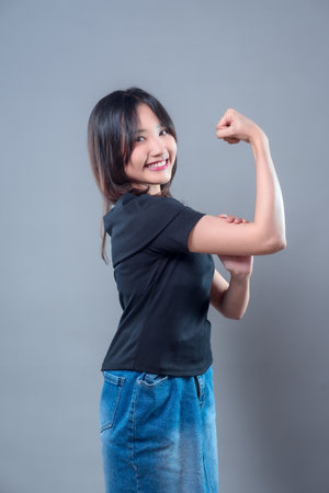 A smiling Asian woman confidently showing her bicep, symbolizing strength and empowerment. Her cheerful expression conveys motivation, positivity, and self-confidence.の写真素材