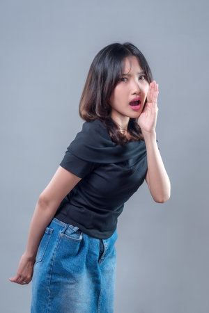 An Asian woman in casual outfit shouting with her hand beside her mouth, showing a surprised and expressive emotion. Suitable for concepts of announcement, communication, and attention.の写真素材