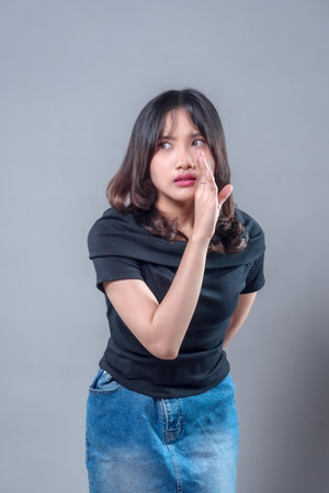 An Asian woman with a curious expression leaning forward and whispering with her hand beside her mouth. The image conveys communication and human emotion in daily life.の写真素材