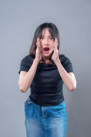 An Asian woman with a surprised expression shouting with both hands beside her mouth. The image represents communication, urgency, announcement, and emotional reaction in modern lifestyle.の写真素材