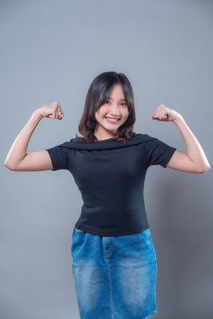 A happy Asian woman confidently smiling while flexing both arms, symbolizing empowerment, success, and motivation. Her positive energy reflects strength, determination, and optimism in life.の写真素材