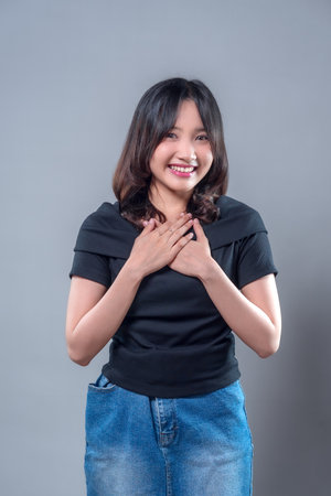 A smiling Asian woman placing her hands on her chest while expressing gratitude and appreciation, showing kindness, sincerity, and positivity in a casual and friendly appearance.の写真素材