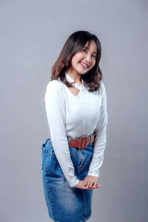 A cheerful young Asian woman smiling warmly with a friendly and natural pose, wearing a white...
