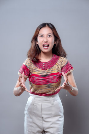 An Asian woman shouts with an open mouth and tense hands, expressing frustration and anger. She...