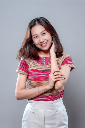 A young Asian woman smiling confidently with a relaxed and natural pose. Wearing a colorful top and light trousers, she radiates warmth, charm, and modern feminine elegance.の写真素材