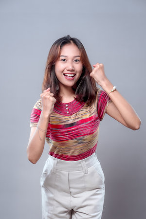 A happy Asian woman smiling brightly while raising her fists in excitement, expressing motivation...