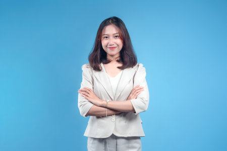 An Indonesian businesswoman standing with a confident smile and arms crossed, wearing formal attire that reflects professionalism and competence in a global corporate environment, conveying leadership and trust.の写真素材