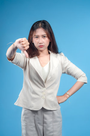 A confident Indonesian businesswoman in formal attire showing a clear thumbs-down gesture with a serious expression, representing disapproval and negative evaluation suitable for global corporate themes.の写真素材