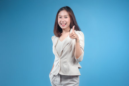 A confident Indonesian businesswoman smiling and giving a thumbs-up gesture while wearing formal attire, presenting a positive, modern, and professional image suitable for global corporate and business themes.の写真素材