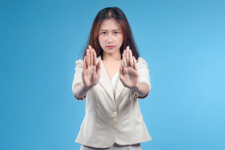 A confident Indonesian businesswoman showing both hands in a stop gesture, with a serious expression and formal attire, presenting a strong and professional image suitable for global corporate and business themes.の写真素材