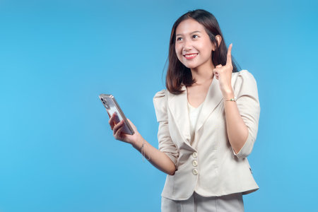 An Indonesian businesswoman in formal attire smiling while holding a smartphone and raising one finger, expressing a bright idea and confidence suitable for global corporate, innovation, and digital business themes.の写真素材