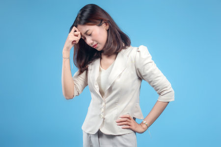 An Indonesian businesswoman showing a thoughtful and slightly stressed expression with her hand on her forehead while wearing formal attire, presenting a professional look suitable for global corporate themes.の写真素材