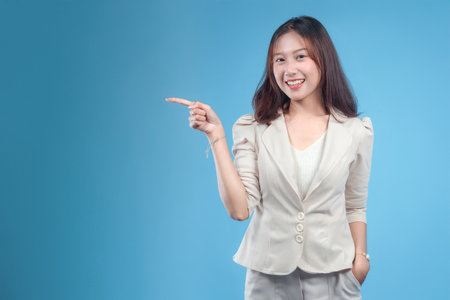 A confident Indonesian businesswoman smiling and pointing to the side, wearing formal attire and expressing a positive, professional attitude suitable for global corporate communication and modern business concepts.の写真素材