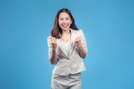 An Indonesian businesswoman smiling confidently while making a strong success gesture with both fists in formal attire, showing a motivated and professional image suitable for global corporate themes.の写真素材