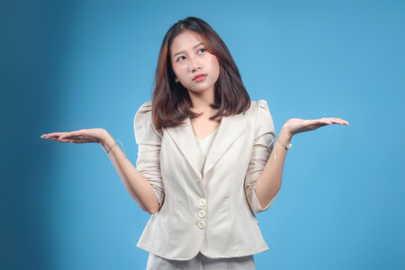 An Indonesian businesswoman displaying an unsure expression with a balanced shrug pose while wearing formal corporate attire, conveying professionalism and relatable decision-making in a global business context.の写真素材