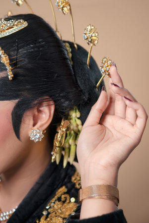 Closeup of Indonesian Javanese bridal details, showing ornate hair ornaments, elegant earrings, refined paes makeup, and delicate hand gesture emphasizing cultural beauty.の写真素材