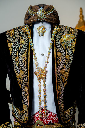 Close up detail of traditional Javanese groom attire featuring black velvet beskap with white shirt,...