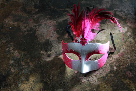 A spotlighted carnival mask on a dark grungy cement floorの写真素材