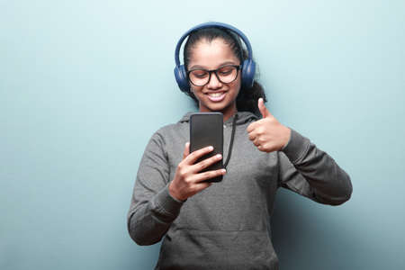 Happy girl of Indian ethnicity with a mobile phone shows thumbs up gesture