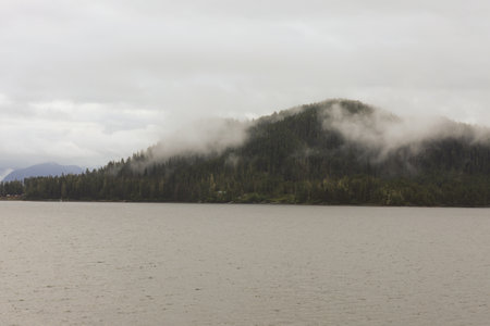 Cruise ship at a port in Juneau, Alaska with snow capped mountain and low lying fog in the...