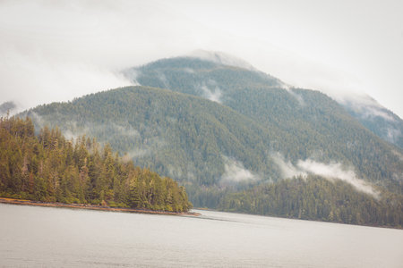 Cruise ship at a port in Juneau, Alaska with snow capped mountain and low lying fog in the...