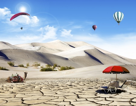 Holiday in the desert: dunes and camel with deck chairs and hot air balloons and paragliding flying in the skyの写真素材
