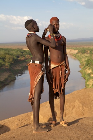 Omo valley, Karo village, Ethiopia, February 16, 2013: african women of the Karo ethnic group show their tribal hairstyle and necklaces with the Omo river in the background. One of them is making the tribal paint on the face of the other.のeditorial素材